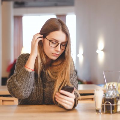 Image of a woman in glasses looking at her phone.